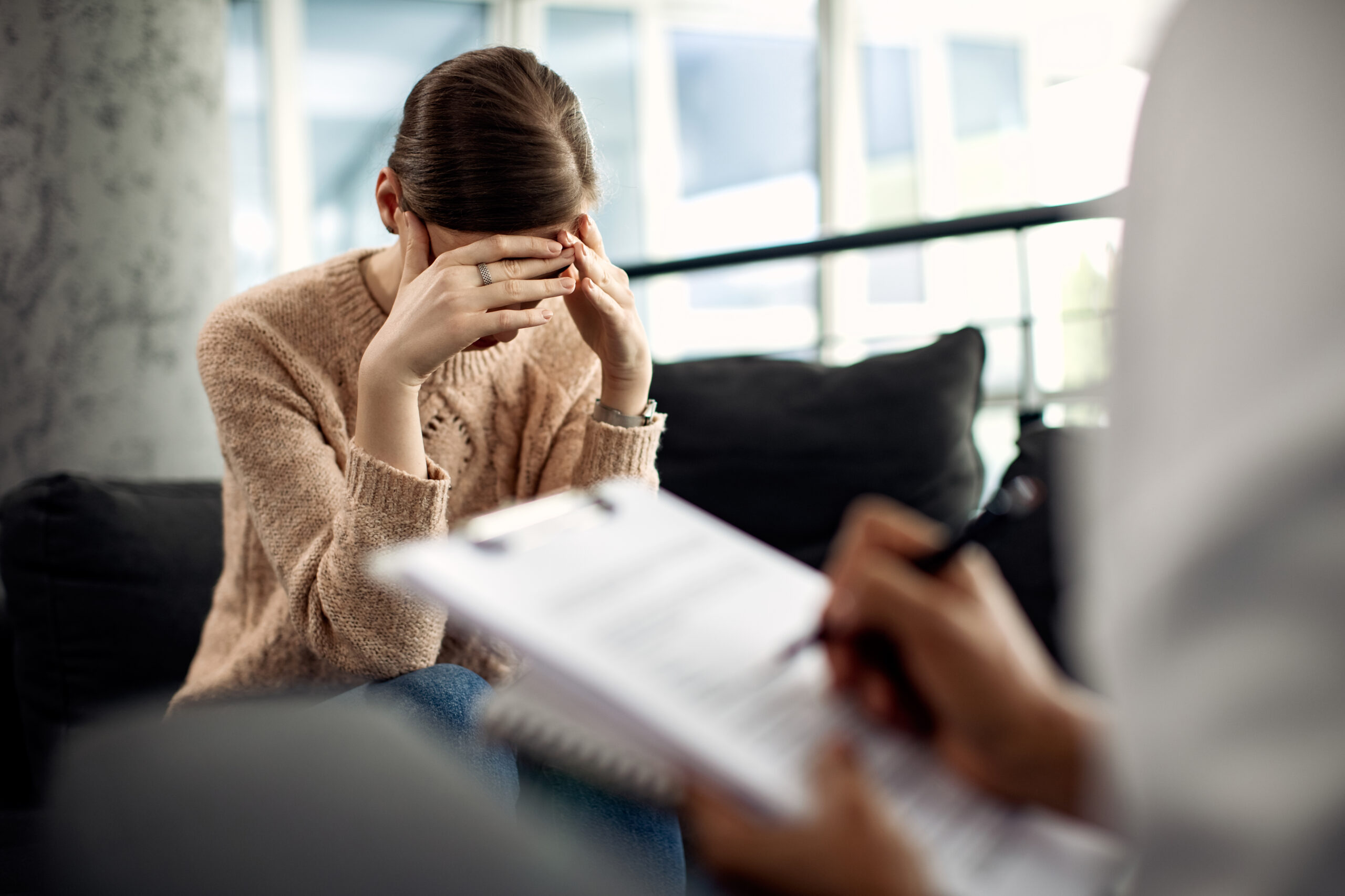 Mulher triste segurando a cabeça com dor emocional enquanto lidacom traumas durante consulta com seu Psicanalista